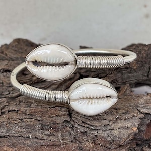 May include: A silver bangle bracelet with two white cowrie shells. The bracelet is made of twisted wire and the shells are attached to the wire.