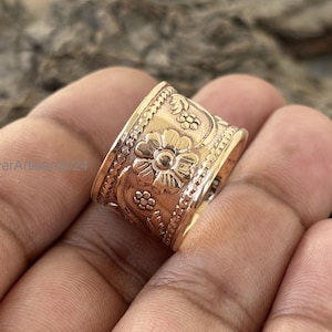 May include: A wide gold-toned ring with a floral design. The ring is made of metal and has a textured surface.