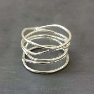 May include: A silver ring with a unique, multi-layered design. The ring is made of thin, twisted wire that creates a modern and abstract look.