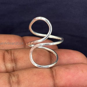 May include: A silver ring with a unique, abstract design. The ring is made of a single piece of wire that is twisted and shaped into a double loop.