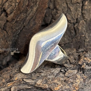 May include: A silver ring with a unique, abstract design. The ring is made of smooth, polished metal and has a wave-like shape.