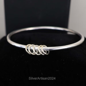 Puede incluir: Un brazalete de plata con un grupo de cinco anillos dorados unidos al centro.