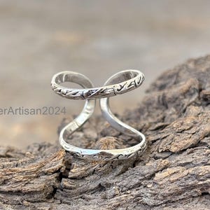 May include: A silver ring with a double band design. The bands are twisted and have a floral pattern.