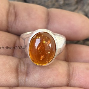 Könnte beinhalten: Ein silberner Ring mit einem ovalen Bernstein. Der Stein hat eine goldene Farbe und ist in eine silberne Fassung gefasst.