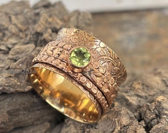 Pode incluir: Um anel giratório de ouro com uma gema verde engastada no centro. O anel é decorado com um padrão floral.