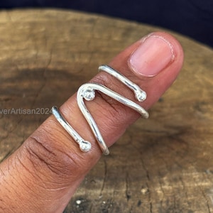 May include: A silver ring with a unique, abstract design. The ring is made of twisted wire with small, round beads at the ends.