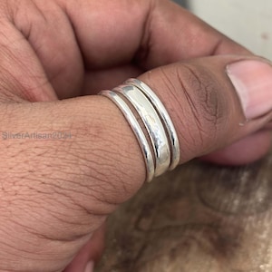 Puede incluir: Un anillo de plata con tres bandas se lleva en un dedo. El anillo tiene una superficie pulida y reflectante. Las bandas están apiladas, creando un efecto de capas. El anillo es una joya.