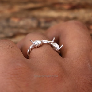 May include: A silver ring shaped like barbed wire. The ring is worn on a person's finger.