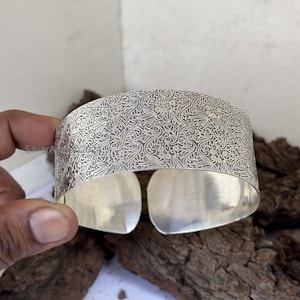 May include: A silver cuff bracelet with an intricate floral pattern etched into the surface.