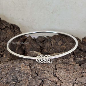 May include: A silver bangle bracelet with a twisted design. The bracelet is made of a single piece of metal and has a smooth, polished finish.