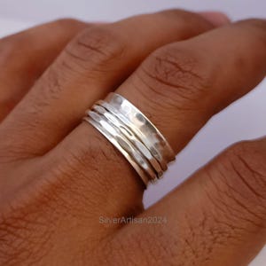 Peut inclure: Une bague tournante en argent avec une finition martelée. La bague est composée de plusieurs bandes qui tournent librement les unes autour des autres.