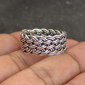 Op de afbeelding: Een zilveren gevlochten ring met een geweven ontwerp. De ring is dik en heeft een brede band.