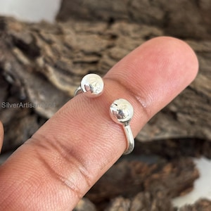 May include: A silver ring with two round balls on the ends. The ring is open and adjustable.