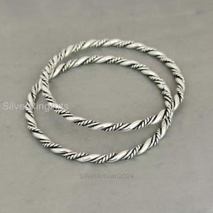 May include: Two silver bangle bracelets with a twisted rope design. The bracelets are stacked on top of each other.