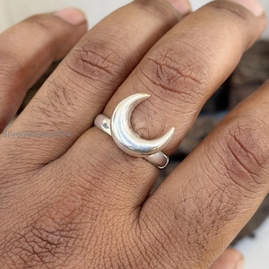 Può includere: Un anello d'argento a forma di mezzaluna. L'anello è indossato su un dito.