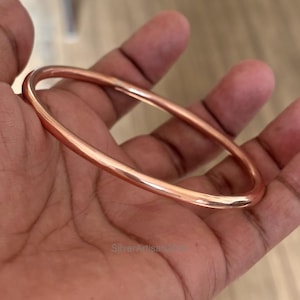 May include: A simple copper bangle bracelet. The bracelet is smooth and shiny, with a warm copper color.