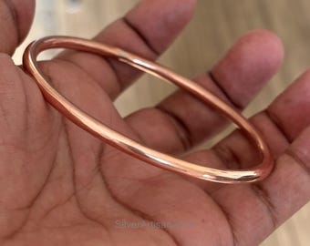 May include: A simple copper bangle bracelet. The bracelet is smooth and shiny, with a warm copper color.