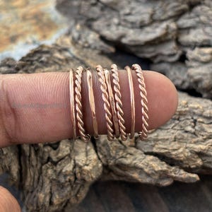 May include: A set of seven rose gold stacking rings. The rings are made of twisted wire and smooth metal.