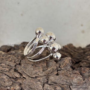 May include: A silver ring with multiple bands and round silver beads. The ring is on a wooden surface.