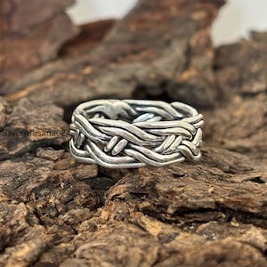 May include: A silver braided ring with a woven design. The ring is made of sterling silver and has a polished finish.