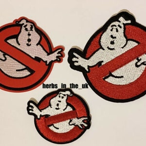 May include: Three embroidered iron-on patches featuring the Ghostbusters logo. The logo is a red circle with a diagonal line through it, and a white ghost figure inside the circle. The patches are different sizes.