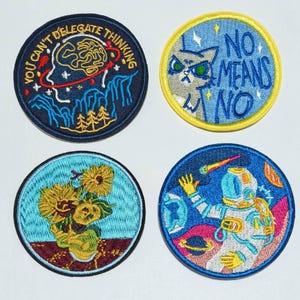 May include: Four embroidered iron-on patches with different designs. The first patch is blue with white and yellow details and says "You can't delegate thinking". The second patch is blue with yellow and white details and says "No means no". The third patch is blue with yellow and white details and features a sunflower design. The fourth patch is blue with yellow, white, and pink details and features an astronaut in space.