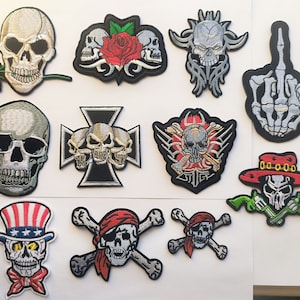 May include: A collection of 11 iron-on patches featuring various skull designs. The patches are in a variety of colours, including black, white, red, green, and blue. Some of the skulls are wearing hats, while others have flowers or other designs around them. The patches are perfect for adding a touch of personality to clothing, bags, or other items.