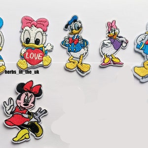 Peut inclure: Ensemble de patchs brodés thermocollants représentant des personnages Disney, dont Donald Duck, Daisy Duck et Minnie Mouse. Les patchs sont colorés et présentent différents motifs, comme Donald Duck tenant un cœur sur lequel est inscrit "LOVE" et Minnie Mouse portant une robe rouge.