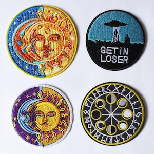 May include: Four embroidered patches with celestial and alien themes. One patch features a sun and moon design in yellow, orange, and blue. Another shows an alien abduction scene with the text "GET IN LOSER." The other two patches have similar designs.