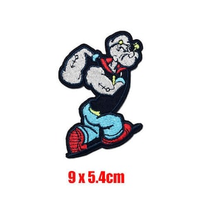 May include: An embroidered iron-on patch featuring a cartoon sailor with a blue and black sailor suit, red shoes, and a white hat. The patch is 9 x 5.4 cm.