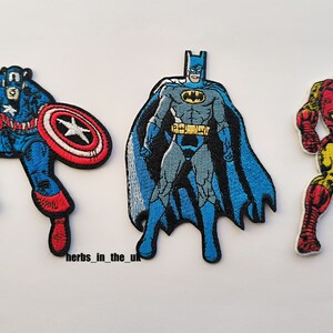 Op de afbeelding: Drie geborduurde strijkpatches met superheldenfiguren: Captain America in blauw en rood, Batman in blauw en grijs en Iron Man in rood en goud.