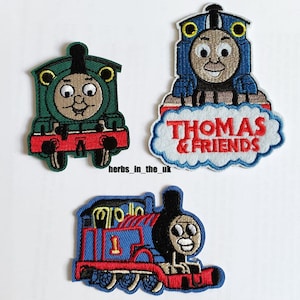 Può includere: Tre toppe ricamate da stirare con i personaggi di Thomas e i suoi amici. Le toppe sono blu, verdi e rosse con dettagli bianchi. Il testo "Thomas & Friends" è sulla toppa blu.