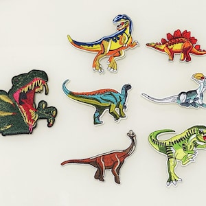 Könnte beinhalten: Set mit 7 aufbügelbaren Stick-Dinosaurier-Patches. Die Patches zeigen verschiedene Dinosaurier in verschiedenen Farben, darunter Grün, Blau, Gelb, Rot und Orange.