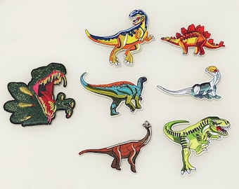 Może przedstawiać: Zestaw 7 naszywek z dinozaurami do prasowania. Naszywki przedstawiają różne dinozaury w różnych kolorach, w tym zielonym, niebieskim, żółtym, czerwonym i pomarańczowym.