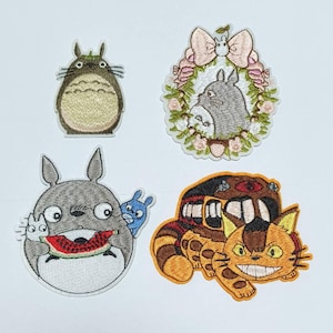 Könnte beinhalten: Vier gestickte Bügelbilder mit Figuren aus dem Animationsfilm 'Mein Nachbar Totoro'. Die Patches zeigen Totoro, der eine Wassermelone isst, Totoro mit einem Katzenbus, einen Blumengirlanden mit Totoro und einen stehenden Totoro.