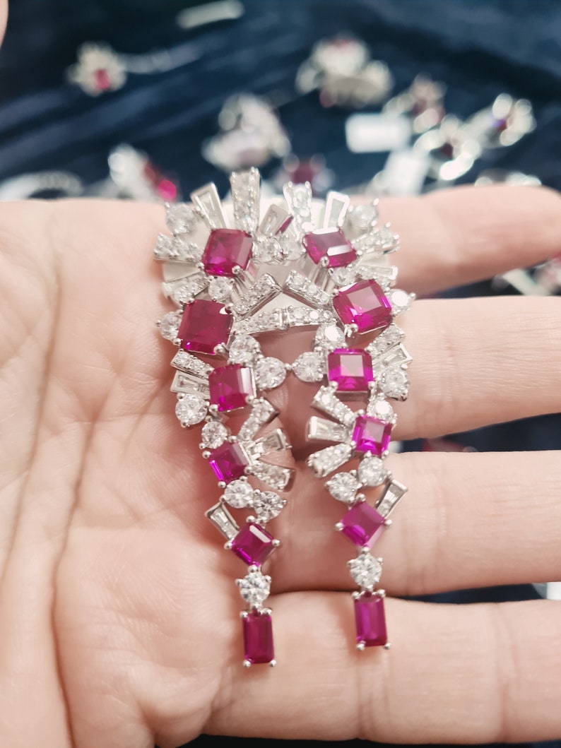 May include: A pair of silver dangle earrings with a cluster of pink and white gemstones. The earrings have a geometric design and are accented with small, sparkling stones.