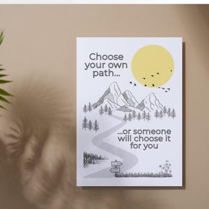 May include: A white print with a yellow sun, mountains, trees, and a winding path. The text says "Choose your own path... or someone will choose it for you."