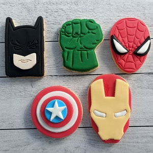 May include: Set of six superhero-themed sugar cookies. The cookies are decorated with colourful icing and feature images of Batman, Hulk, Spiderman, Iron Man, and Captain America.