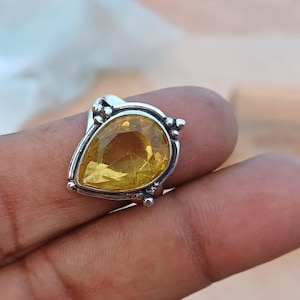 Pode incluir: Um anel de prata com uma gema amarela em forma de pêra engastada em uma moldura de prata decorativa.