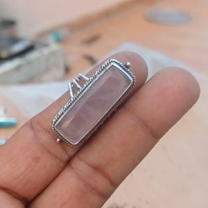 Puede incluir: Un anillo de plata con una piedra rectangular de cuarzo rosa. El anillo tiene una banda de plata detallada.