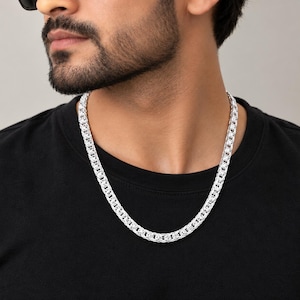 Peut inclure: Un collier chaîne en argent doté d'un motif complexe de maillons byzantins entrelacés. Les maillons métalliques sont polis pour obtenir une finition brillante et réfléchissante, créant un aspect dense et texturé sur un t-shirt noir.