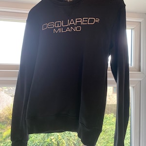 Może przedstawiać: Czarny, dług rękawowy sweter z haftowanym białym logo z napisem "DSQUARED2 MILANO".