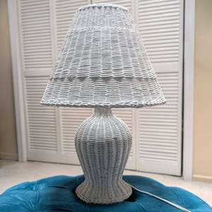 May include: A white wicker table lamp with a woven shade and a bulbous base. The lamp is sitting on a blue ottoman. The lamp's shade is approximately 18 inches in diameter and the lamp is about 30 inches tall.