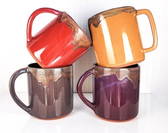 Peut inclure: Quatre tasses en céramique de différentes couleurs, dont le rouge, le marron, le violet et le jaune. Les tasses ont une finition émaillée avec un effet moucheté.