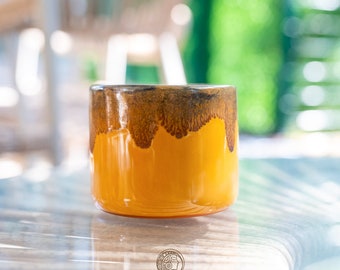 Peut inclure: Une tasse en céramique jaune avec un glaçage brun. La tasse a une forme arrondie et une finition lisse.