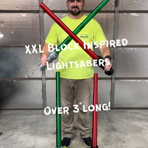 Puede incluir: Dos sables de luz de juguete grandes y de gran tama&ntilde;o, uno verde y otro rojo, se cruzan frente a una persona que lleva una camisa amarilla. Los sables de luz tienen m&aacute;s de 90 cm de largo. El texto "XXL Block Inspired Lightsabers" y "Over 3' Long!" es visible en la imagen.