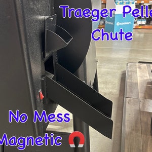 May include: Close-up of a black Traeger pellet chute with a red button and a magnetic flap. The text "No Mess Magnetic" is written in blue below the chute.