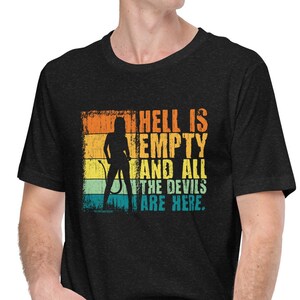 Puede incluir: Una camiseta negra con un gráfico de estilo vintage que dice "El infierno está vacío y todos los demonios están aquí." El gráfico presenta una silueta de una mujer con cola y un fondo rojo con rayas amarillas, naranjas, azules y verdes.