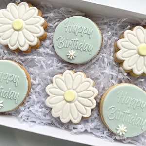 May include: A gift box filled with six decorated sugar cookies. The cookies are decorated with white icing and feature a daisy design and the text "Happy Birthday".