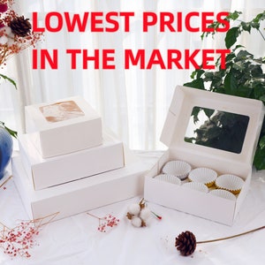 May include: White cardboard boxes with clear windows for packaging cupcakes or other baked goods. The boxes are stacked on top of each other. The text "LOWEST PRICES IN THE MARKET" is written in red letters on a white background.
